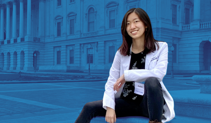 Anna Li sitting on steps outside of a government building wearing her white coat.